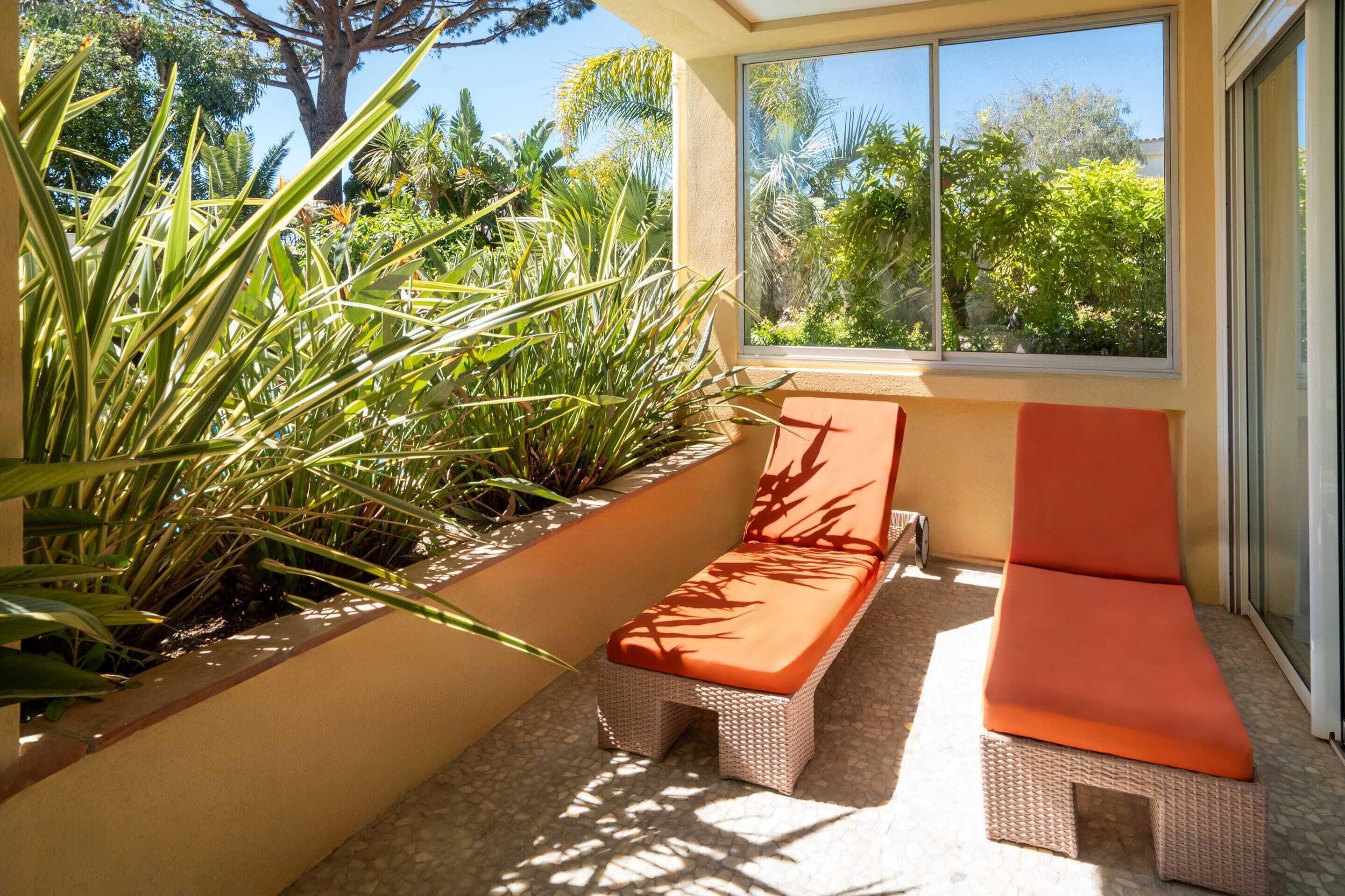 A sunlit outdoor seating area with wicker furniture and a view of lush greenery.
