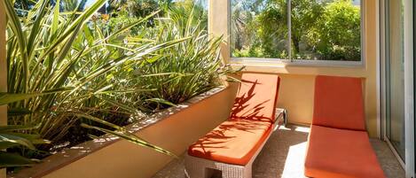 Un área de estar al aire libre iluminada por el sol, con muebles de mimbre y vistas a exuberante vegetación.