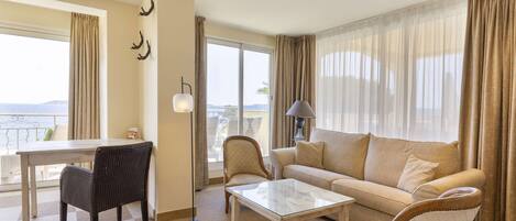 Habitación de hotel con comedor, sofá, mesa de centro y vistas al mar.