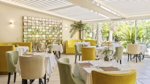 Un restaurant avec des chaises jaunes et vertes, des tables blanches et un grand mur recouvert de tableaux encadrés.
