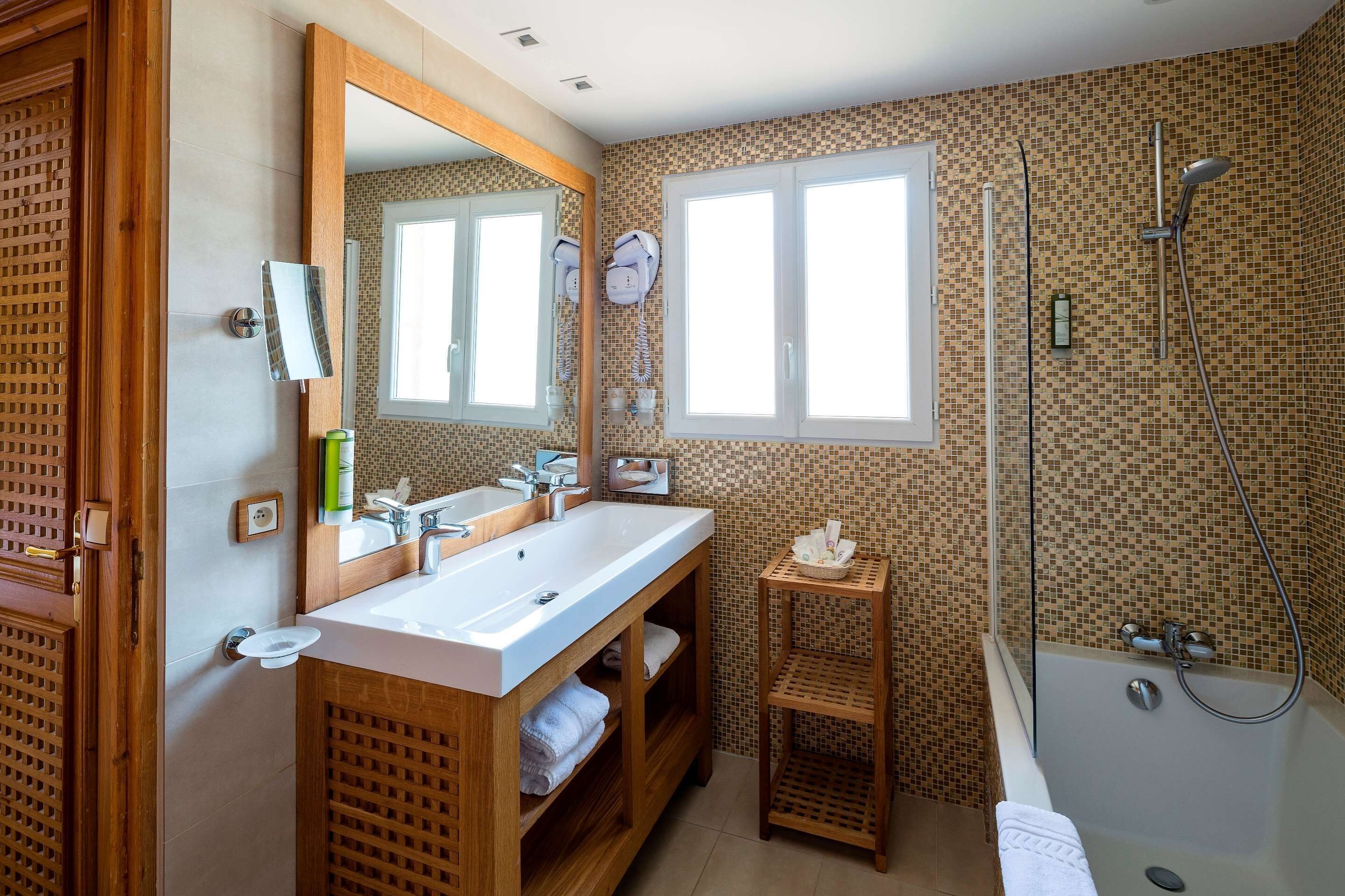 A bathroom with two sinks, a large mirror, a shower, and a small shelf.