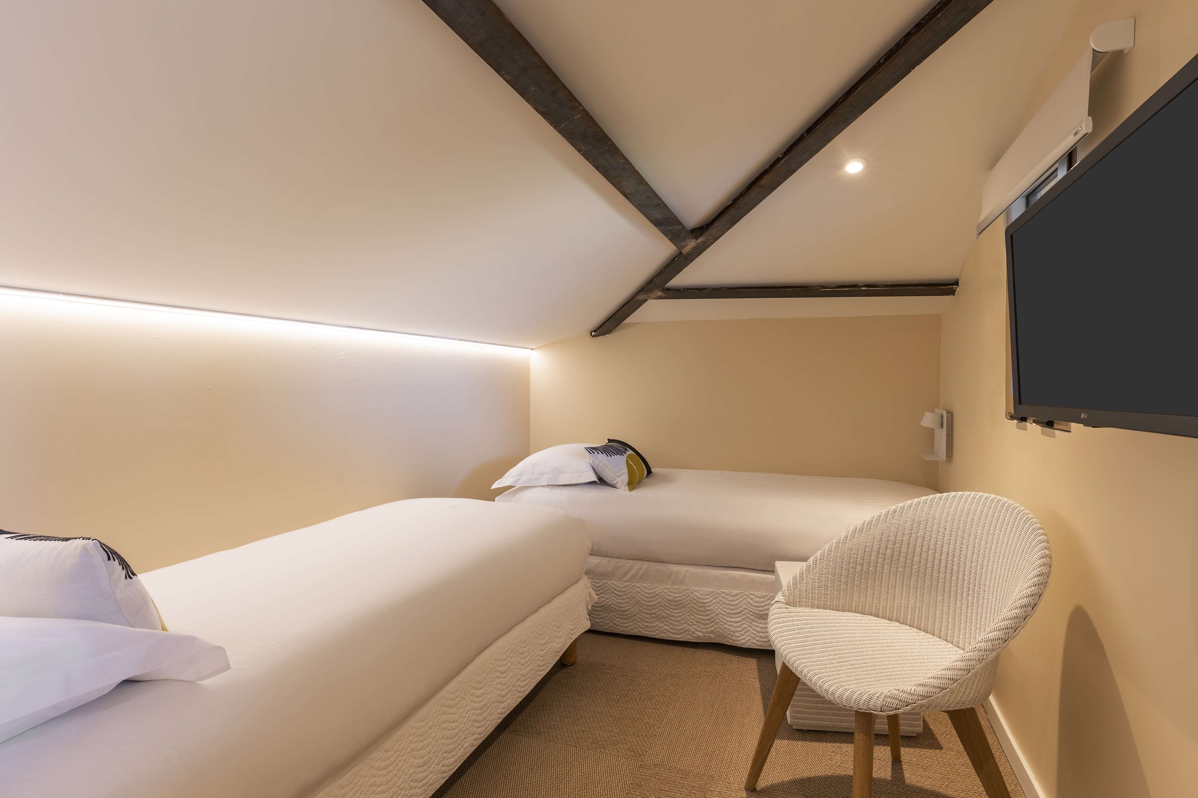 A small, cozy room with two beds, a chair, and a mounted TV.