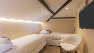 A small, cozy room with two beds, a chair, and a mounted TV.