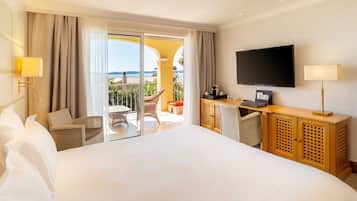 A hotel room with a large bed, a desk with a flat-screen TV, a chair, and a view of the ocean.