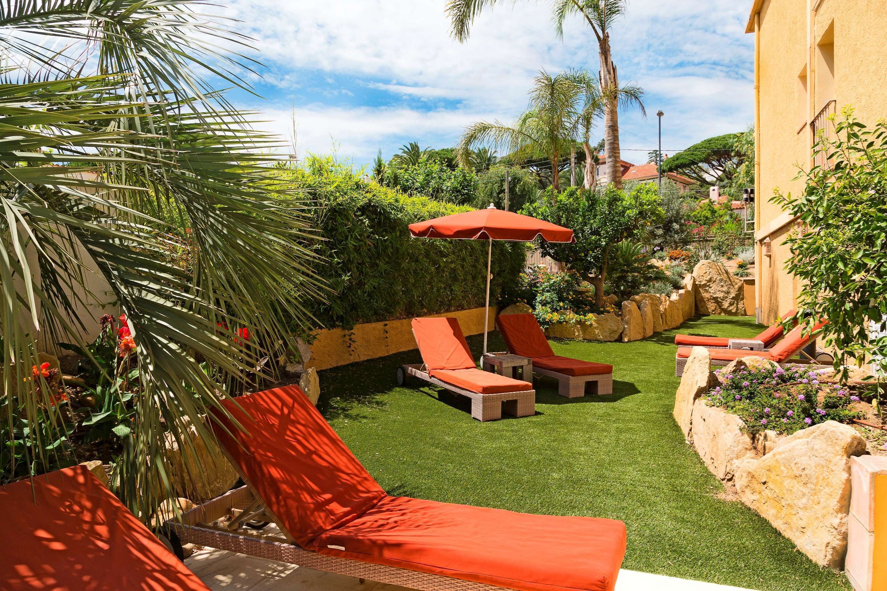 Un jardín bien cuidado con césped artificial, mobiliario exterior y una variedad de plantas y árboles.
