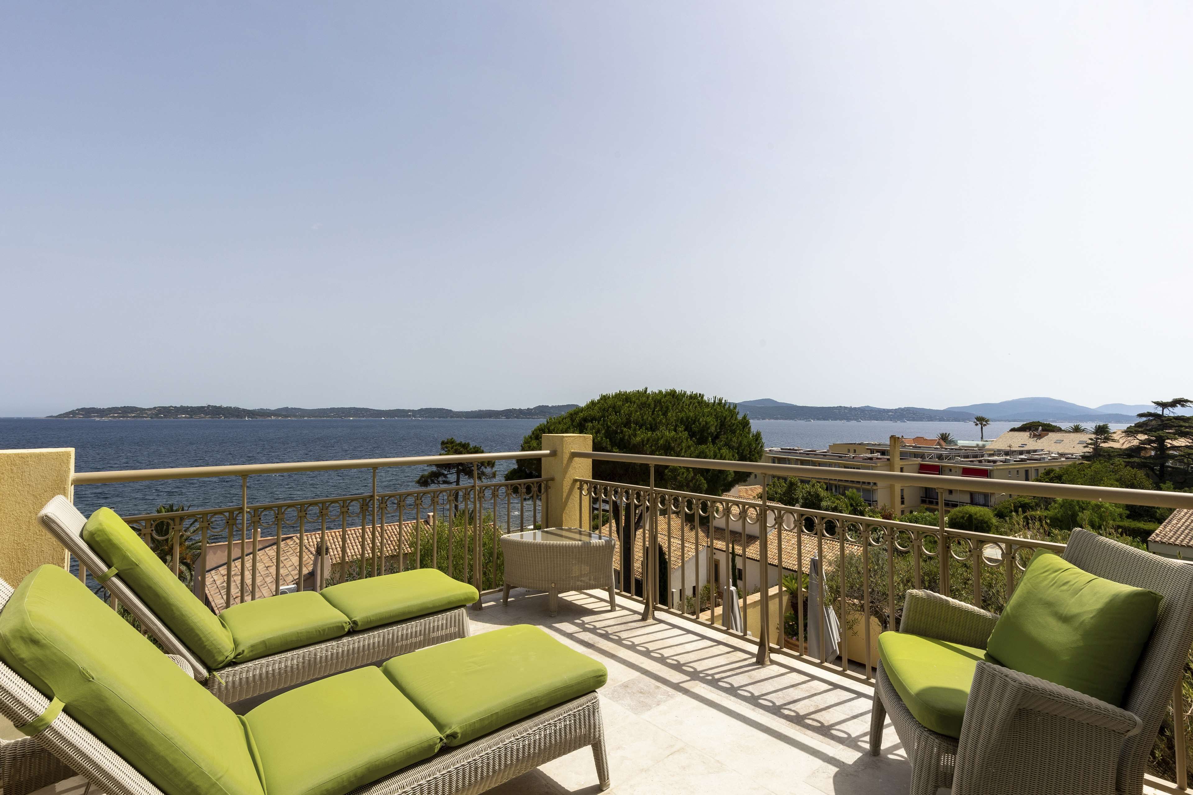A balcony with wicker furniture, a view of the sea, and distant mountains.