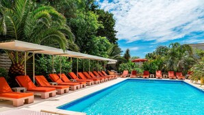 Une piscine entourée d’une végétation luxuriante, avec des chaises longues et des parasols.