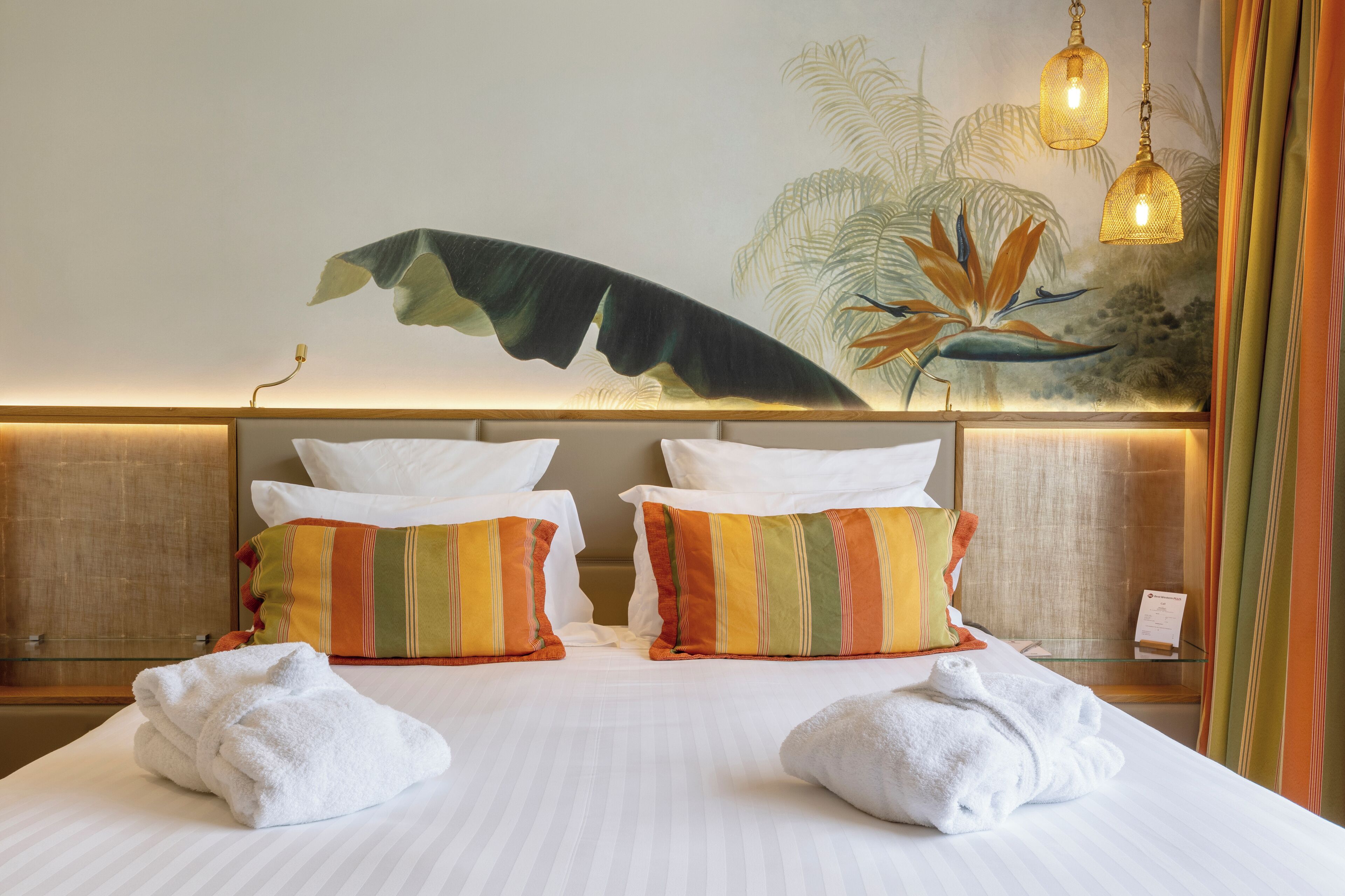 Une chambre d’hôtel équipée d’un lit, d’oreillers, de serviettes, d’une fresque murale et d’un luminaire suspendu.