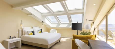 Habitación de hotel moderna con tragaluz, cama, escritorio, silla y vista al mar.