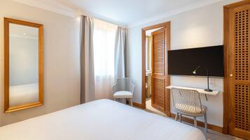 A hotel room with a bed, a desk with a chair, a television, and a large mirror.