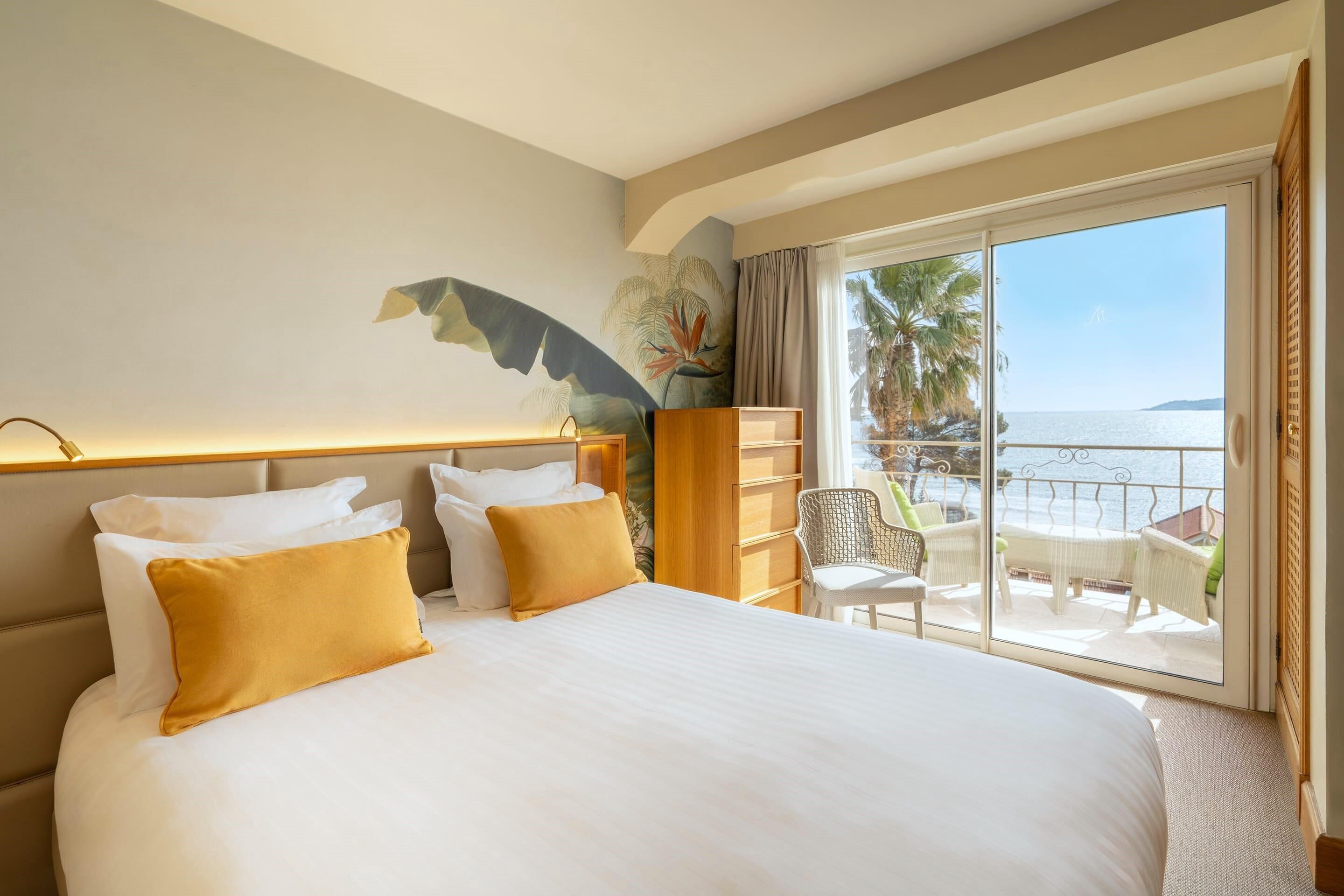 Una camera d'albergo con un letto grande, un comodino, una sedia, un armadio in legno e un balcone vista mare.