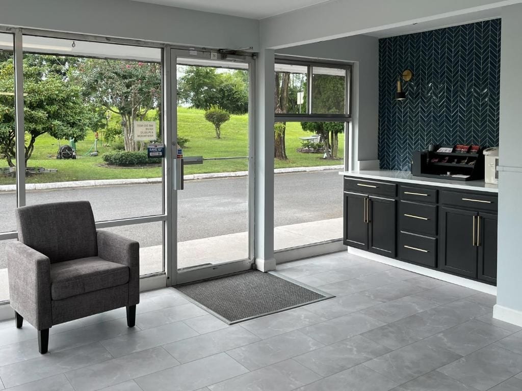 Un interior moderno con un divisor de vidrio corredero que da a un jardín, un sillón gris y una cocina negra con salpicadero de espiga.