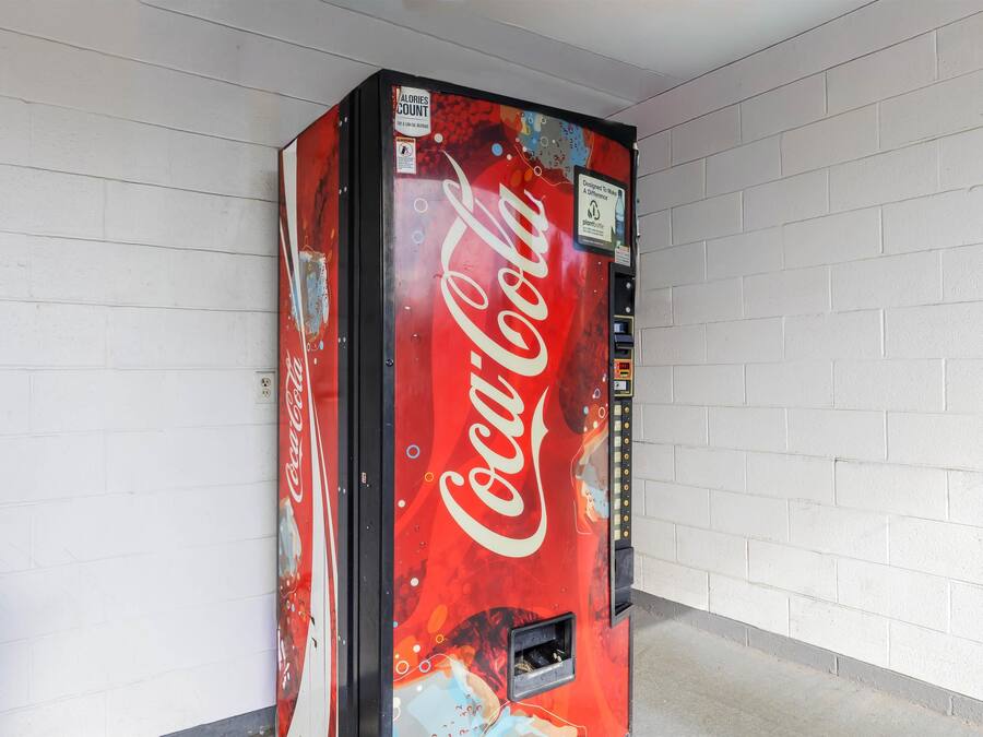 A Coca-Cola vending machine in a hallway with white brick walls.