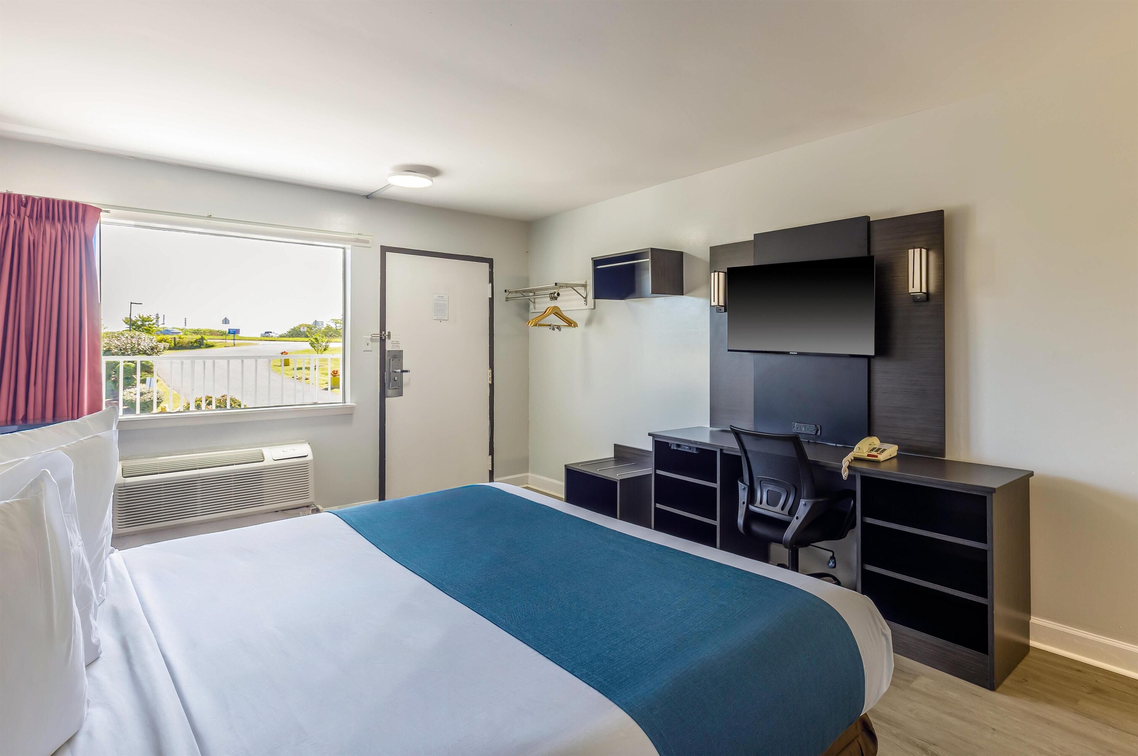 Habitación de hotel con cama, escritorio, silla, televisor y ventana con vistas al exterior.