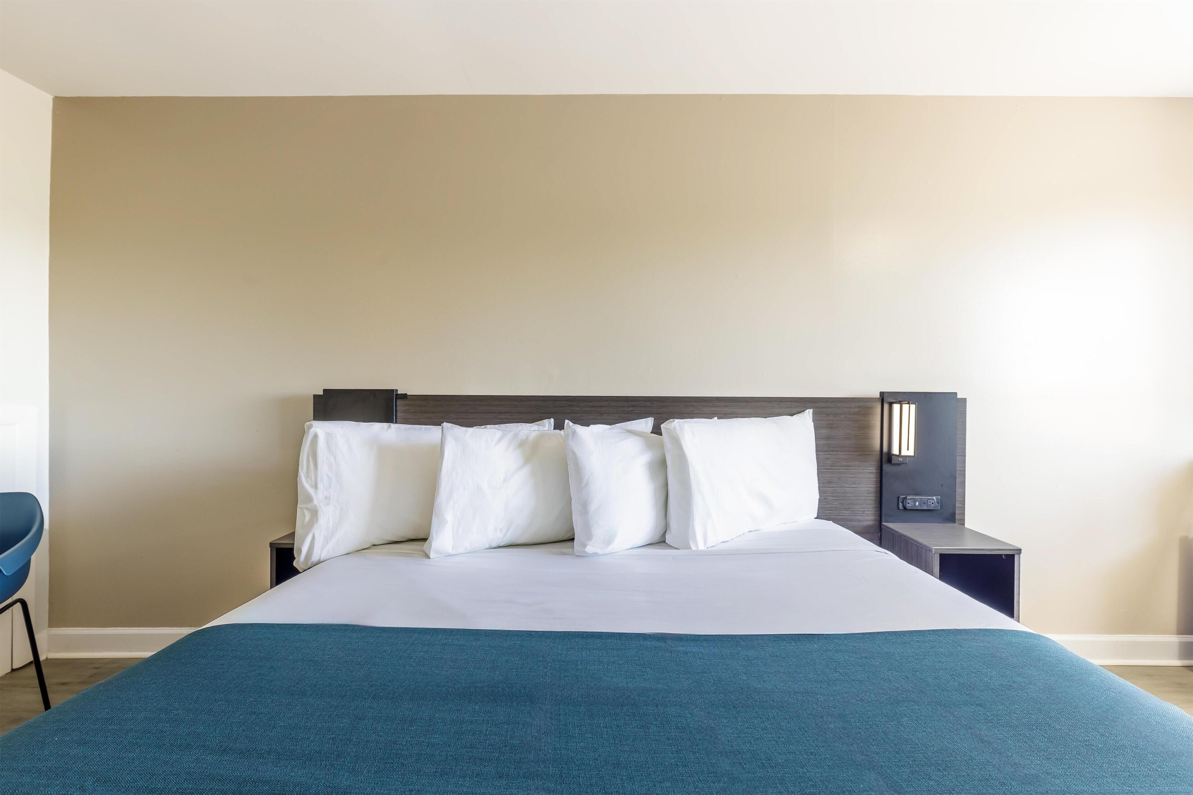A neatly made bed with white and teal bedding, a wooden headboard, and a small bedside table with a lamp.