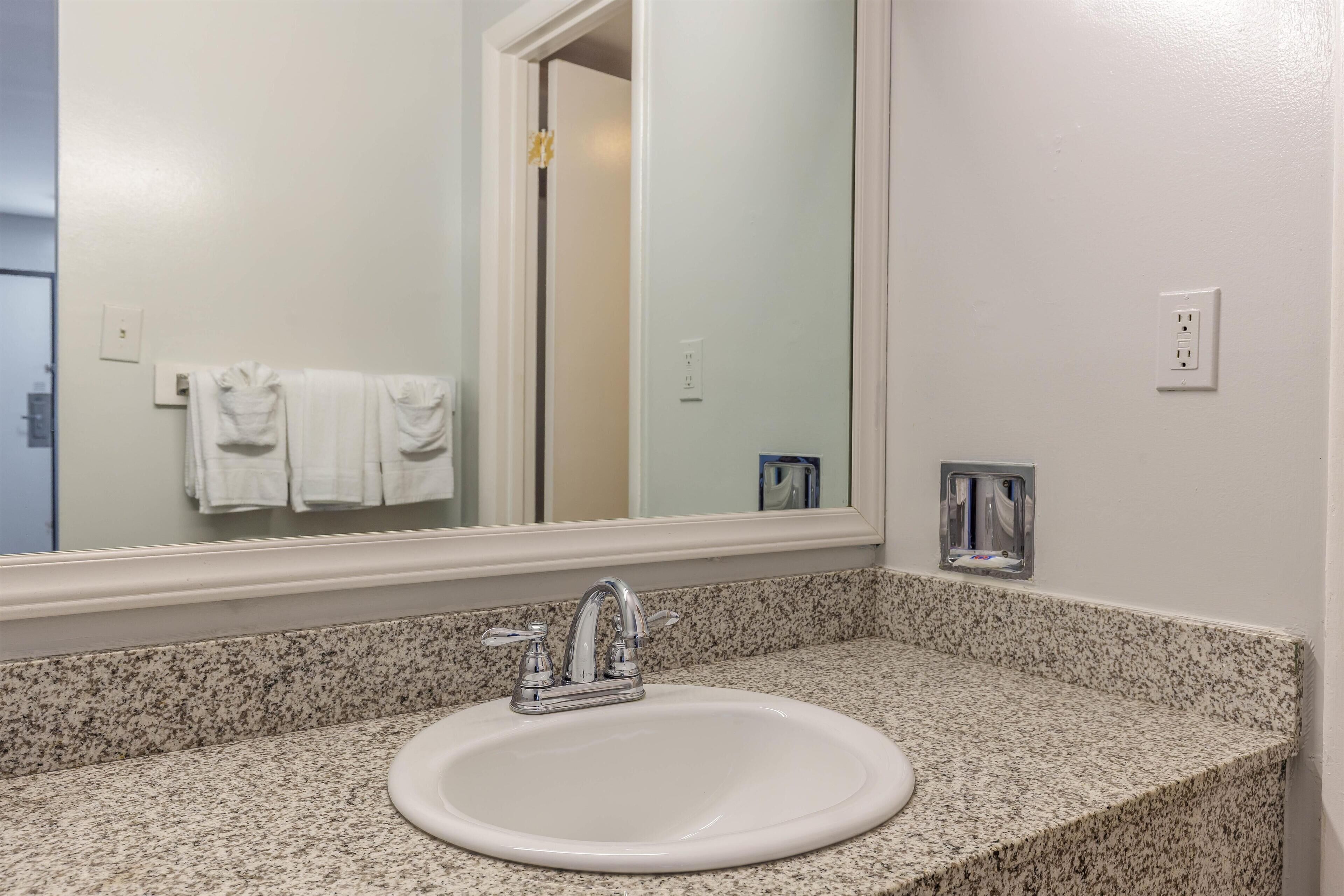 A bathroom with a granite countertop, a white sink, a mirror, and a towel rack with white towels.