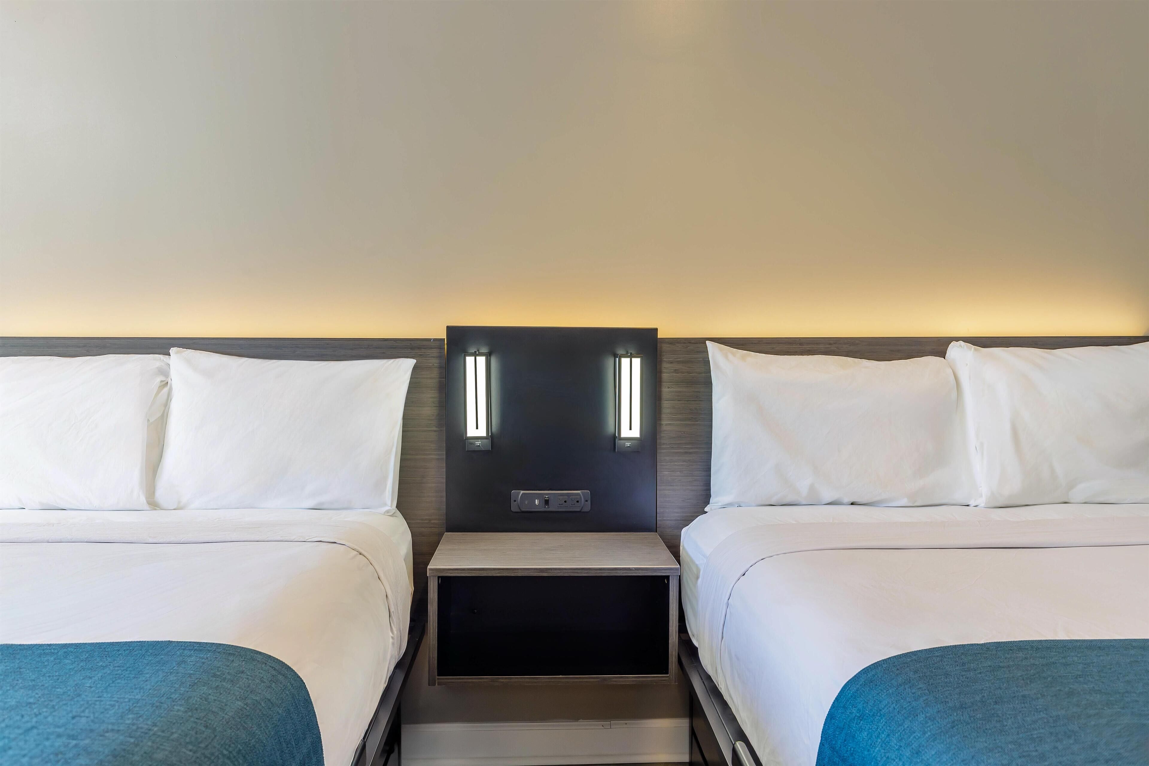 Ein Hotelzimmer mit zwei Betten, einem Nachttisch dazwischen und einer Wandleuchte.