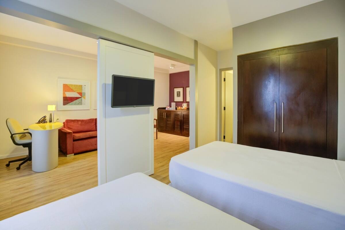 Una habitación de hotel con cama, escritorio, silla, televisor y armario.