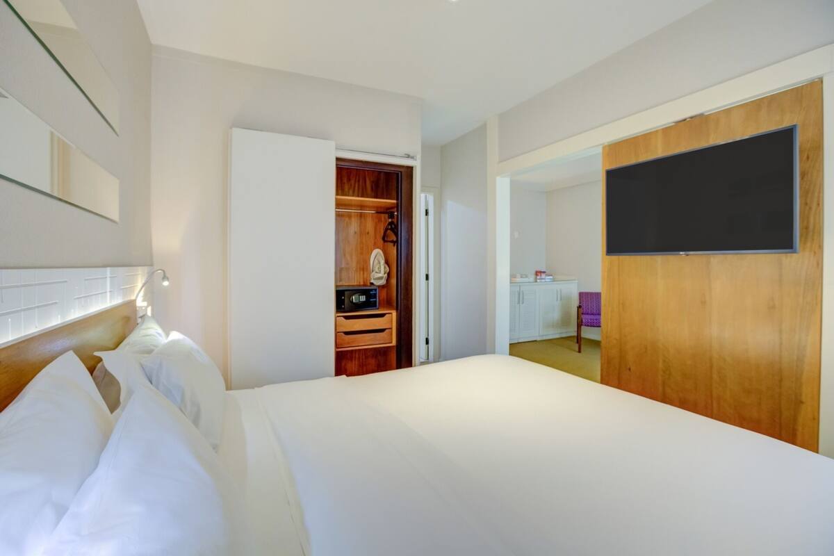 Una habitación de hotel con cama, un armario de madera, televisión y kitchenette.