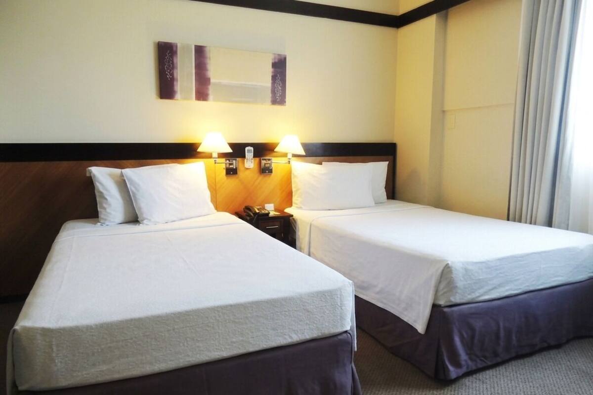 Una habitación de hotel con dos camas individuales, cabecero de madera, lámparas de noche y una obra de arte colgada en la pared.