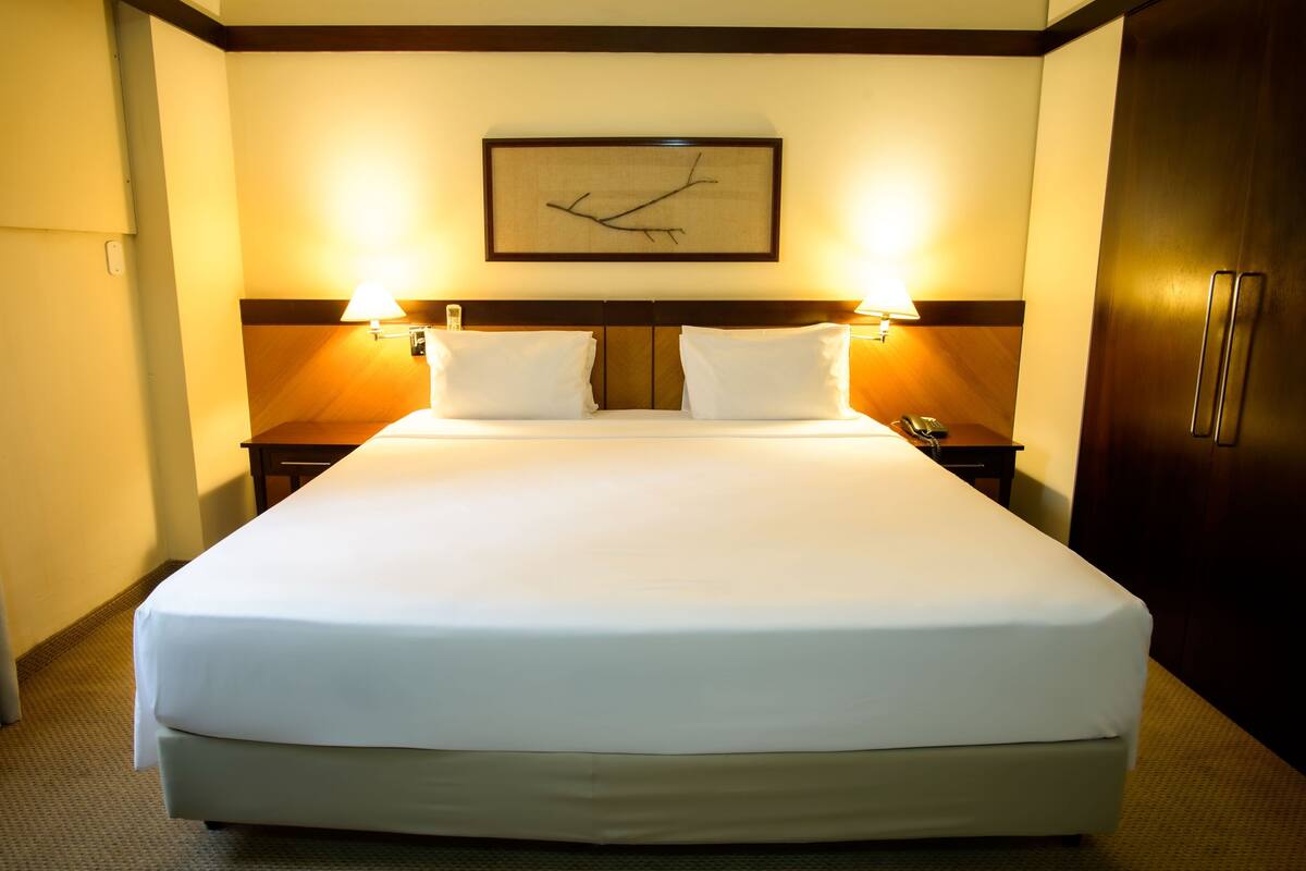 Habitación de hotel con una cama grande, dos mesitas de noche con lámparas, un cabecero de madera y un cuadro enmarcado en la pared.