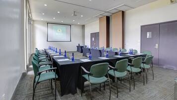 A conference room with a long table, green chairs, and a projector screen displaying 'Quality Assurance'.