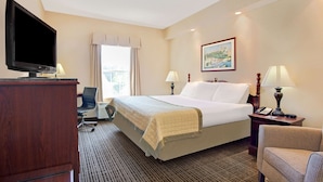 A hotel room with a bed, a desk with a television, two lamps, a chair, and a painting on the wall. - Baymont by Wyndham Pearl (Pearl)