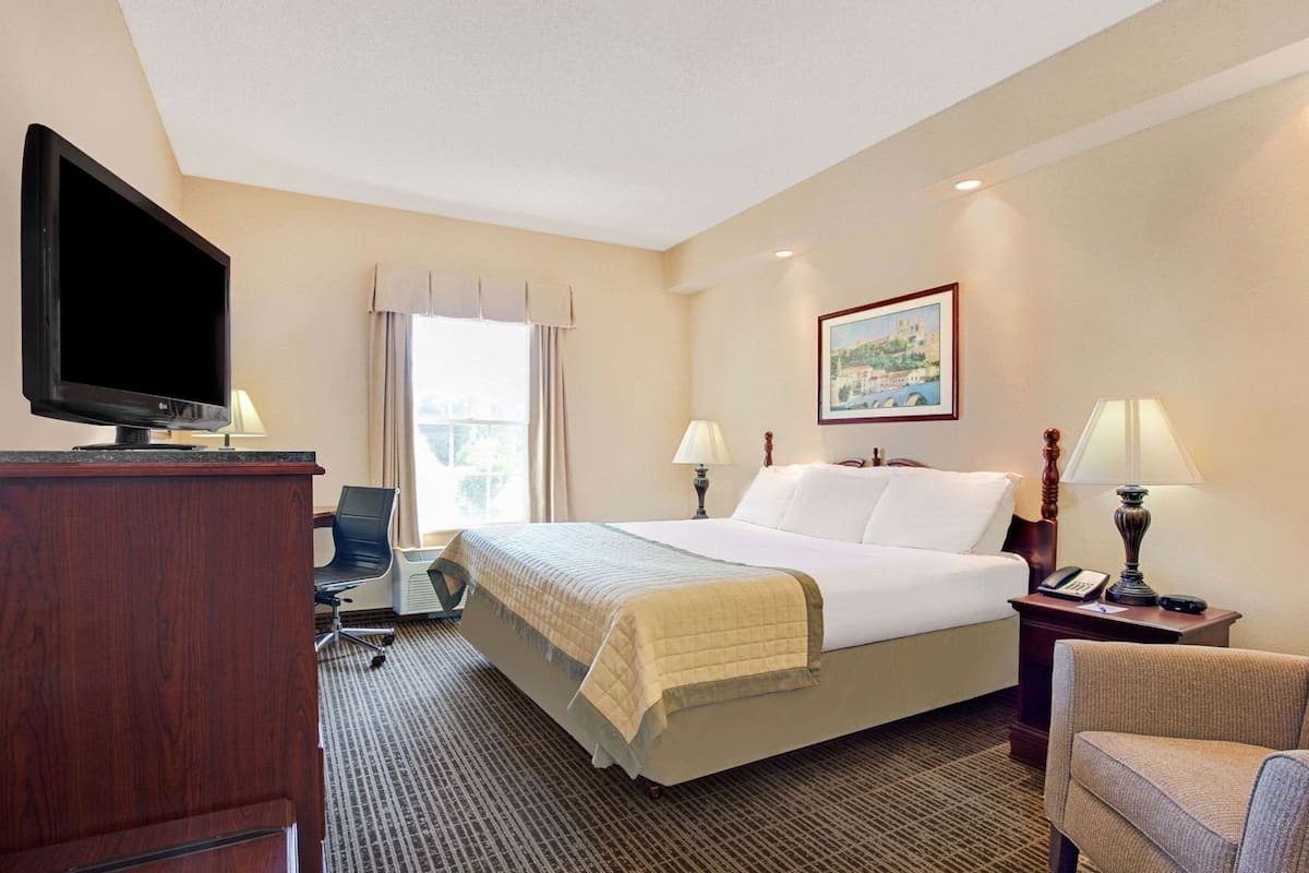 A hotel room with a bed, a desk with a computer, a TV, a chair, and a lamp.
