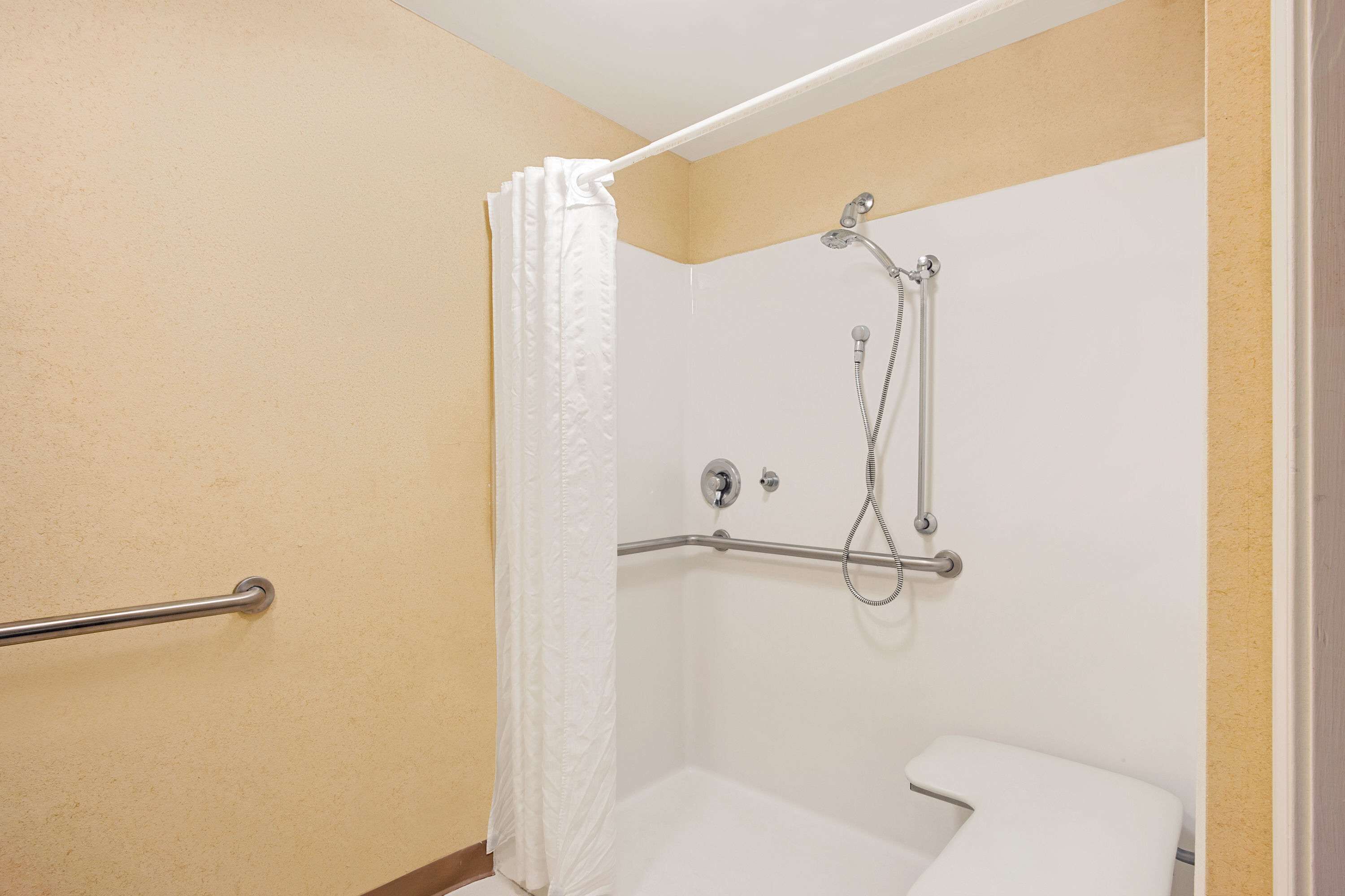 A small, single-person shower with a grab bar, a white toilet, and a shower curtain.