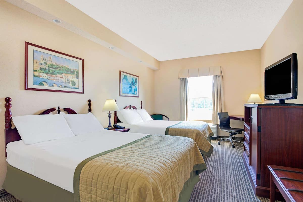 A hotel room with two beds, a desk, a chair, a television, and artwork on the walls.