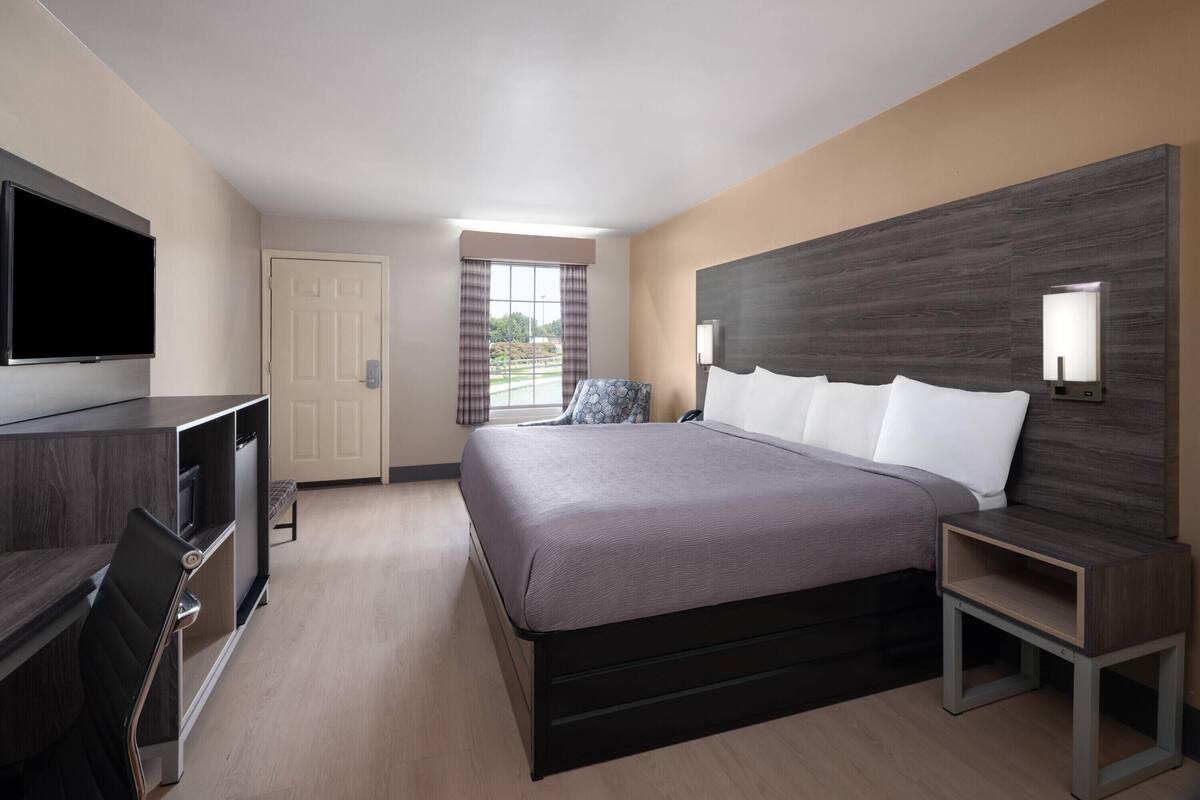 Ein Hotelzimmer mit Bett, Fernseher, Schreibtisch und einem Vorhangfenster.