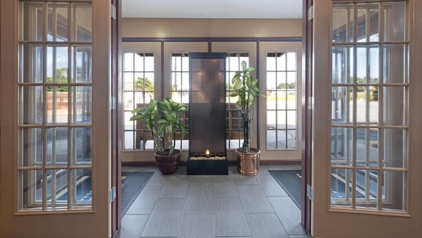 Een hotel lobby met een centraal haardvuur, grote ramen en potplanten.