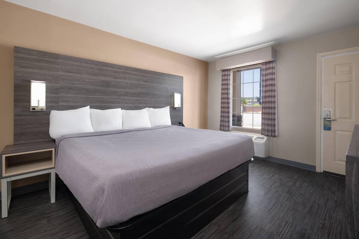 Ein modernes Hotelzimmer mit einem großen Bett, einem Nachttisch, einem Fenster mit Vorhängen und einer Tür.
