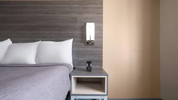 A neatly made bed with white linens, a small bedside table with a lamp, and a wall-mounted light fixture.
