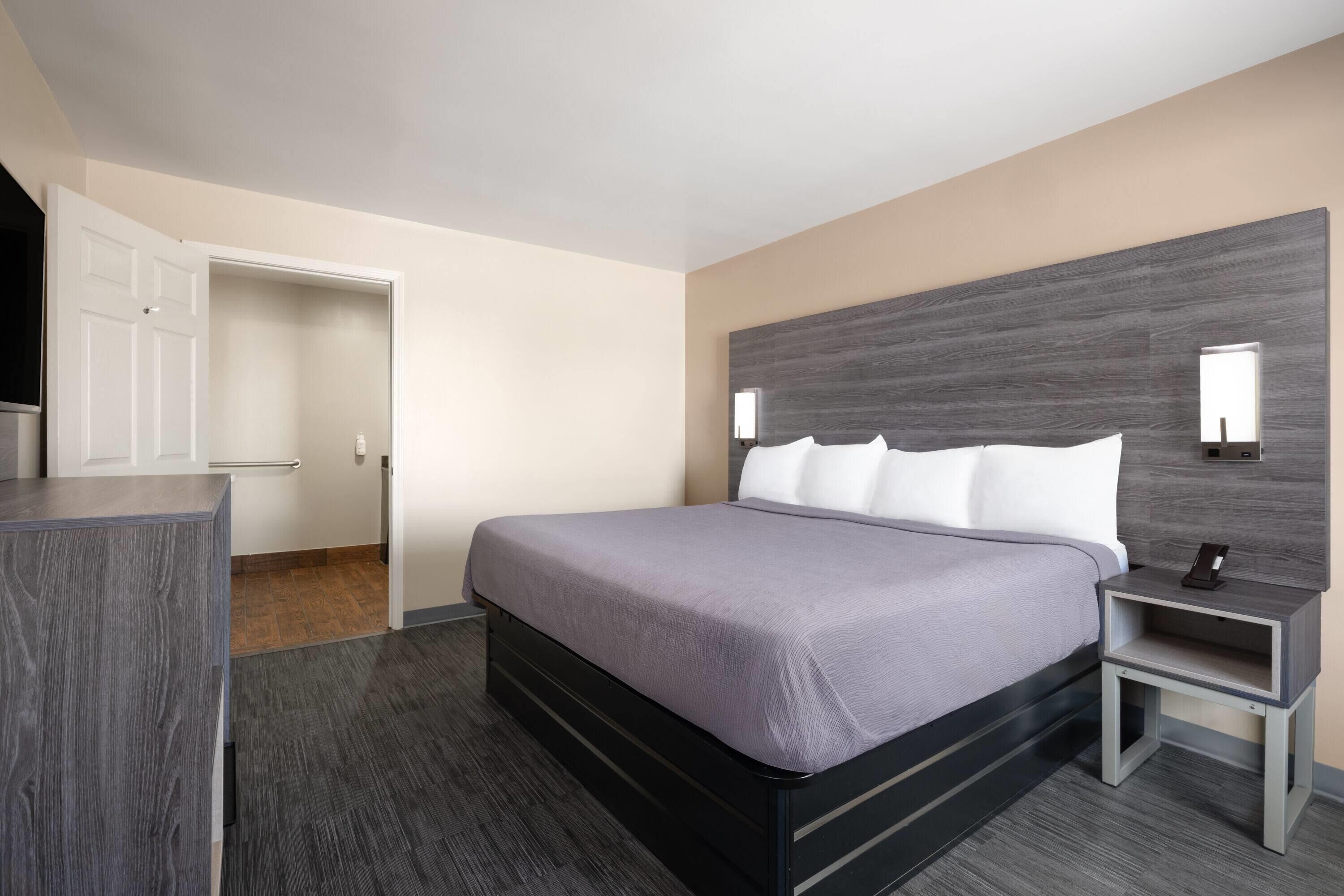 A modern hotel room with a large bed, a bedside table, a wardrobe, and a mirror.