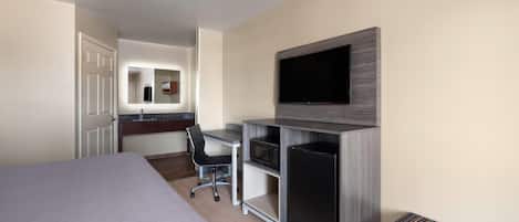 Habitación de hotel con una cama grande, un escritorio con silla, un televisor en la pared y un refrigerador pequeño.