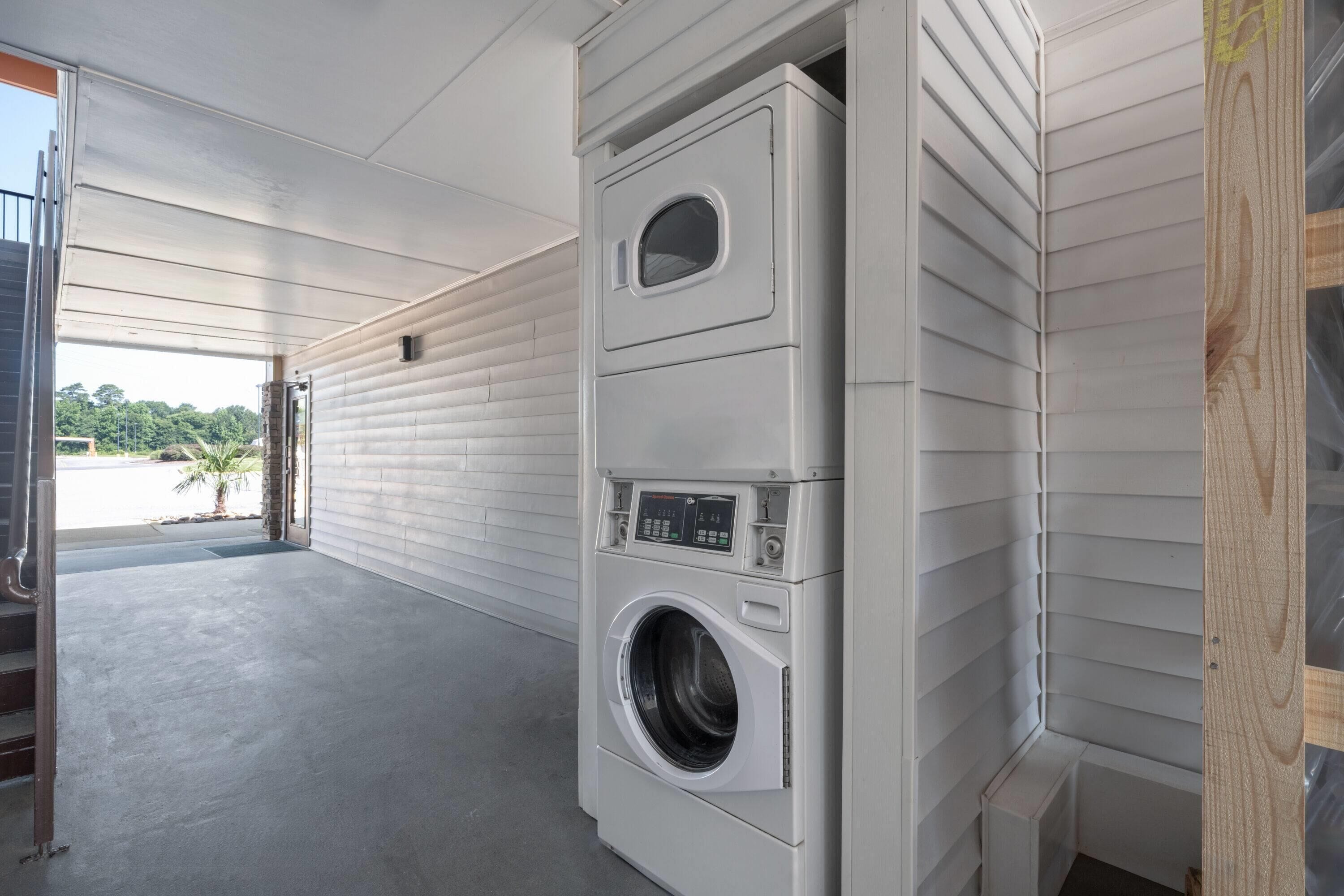 Un cuarto de lavandería con dos lavadoras y secadoras apiladas, piso de concreto y vista al exterior.
