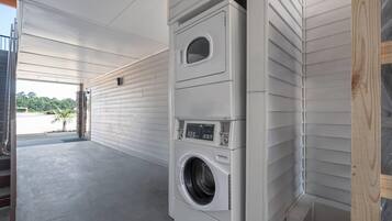 Un cuarto de lavandería con dos lavadoras y secadoras apiladas, piso de concreto y vista al exterior.