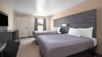 Habitación de hotel con dos camas, un escritorio, un televisor y una ventana con cortinas.