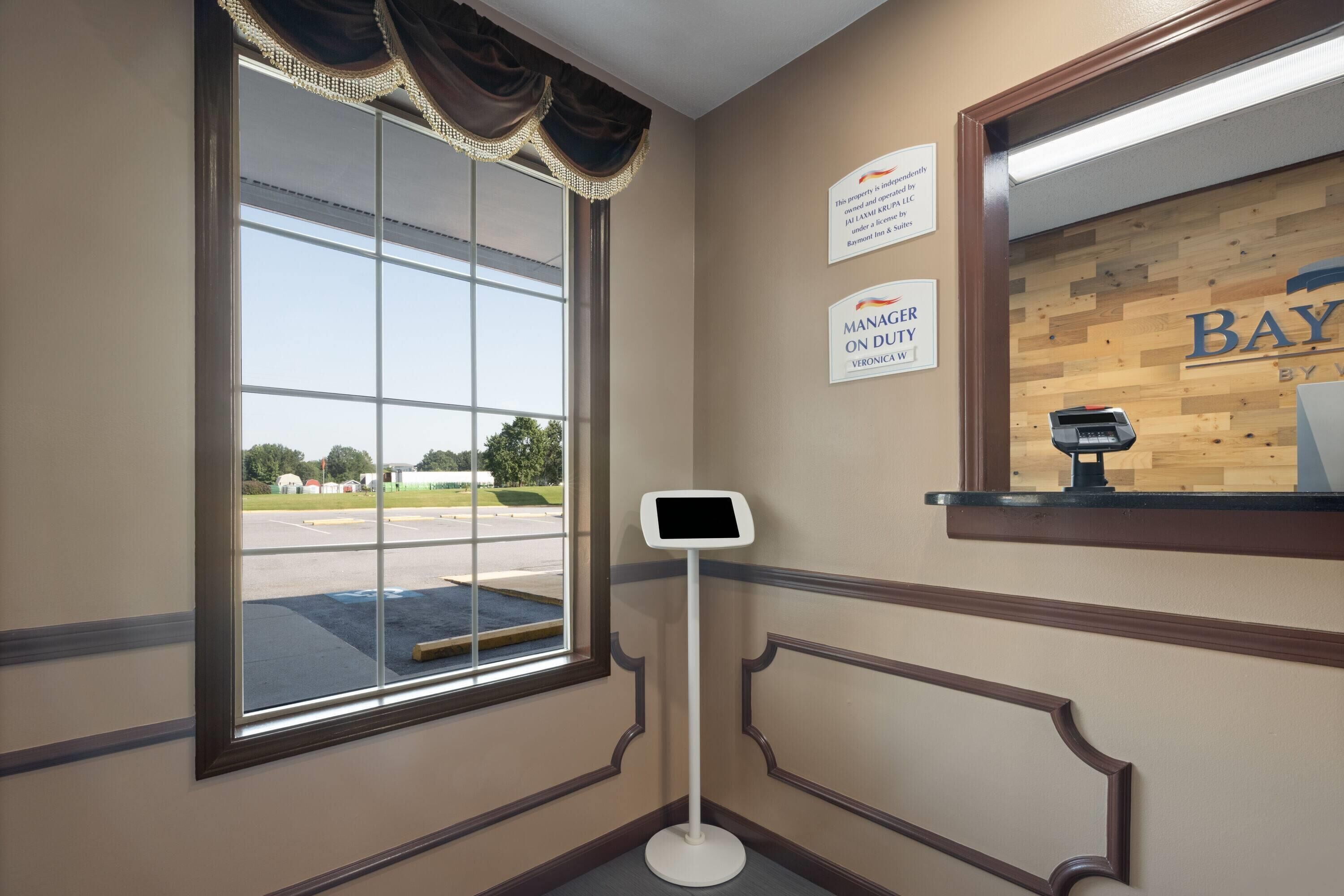 A reception area with a large window, a digital kiosk, and a wooden wall with a sign that reads "Manager on Duty Veronica".