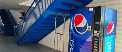 A Pepsi vending machine next to a blue staircase in a commercial setting.