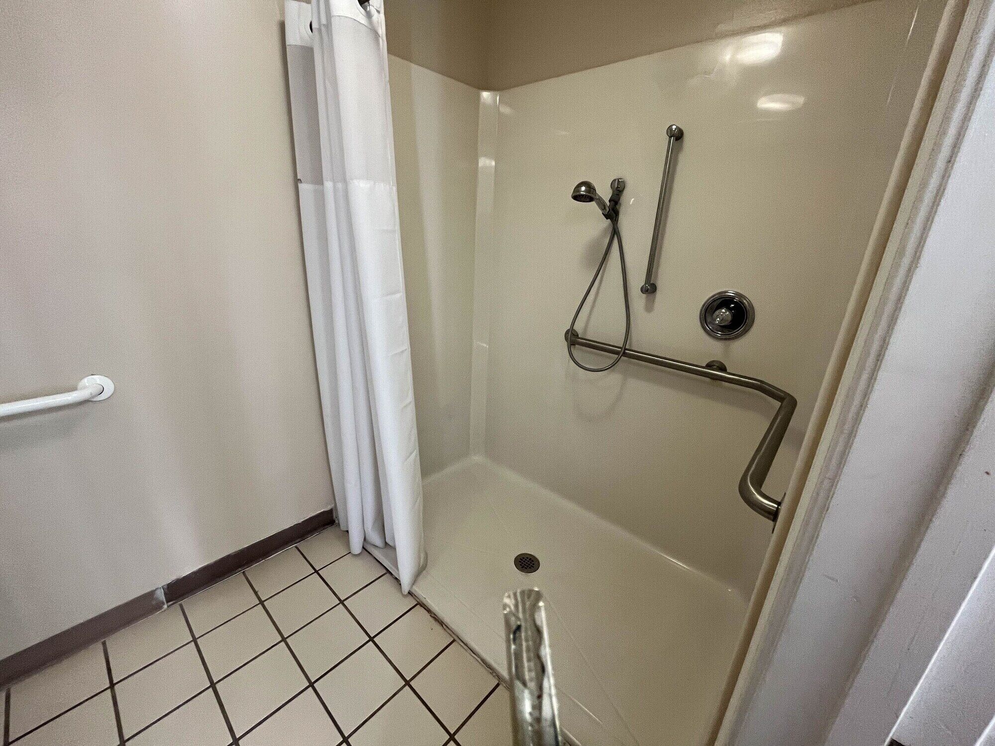 A small, enclosed shower area with a grab bar, a white curtain, and a tiled floor.