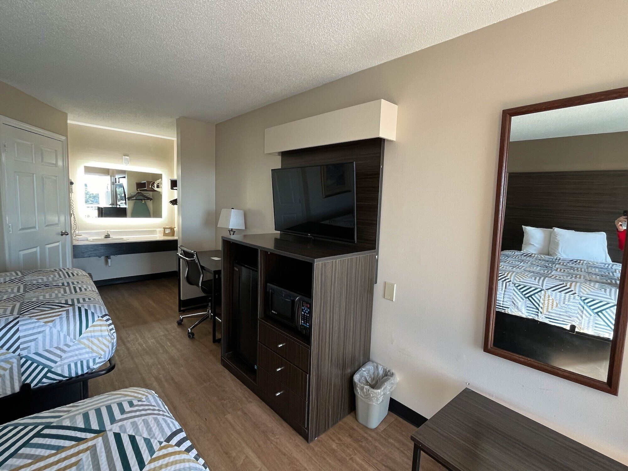 Habitación de hotel con dos camas, un escritorio con televisor, un espejo y un cesto de basura.