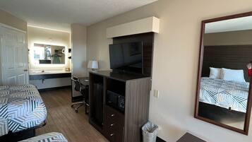 Habitación de hotel con dos camas, un escritorio con televisor, un espejo y un cesto de basura.