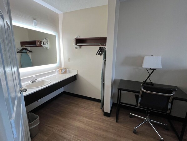 A hotel bathroom with a sink, mirror, towel rack, and a desk with a lamp. - Motel 6 Georgetown, SC - Marina (Georgetown)