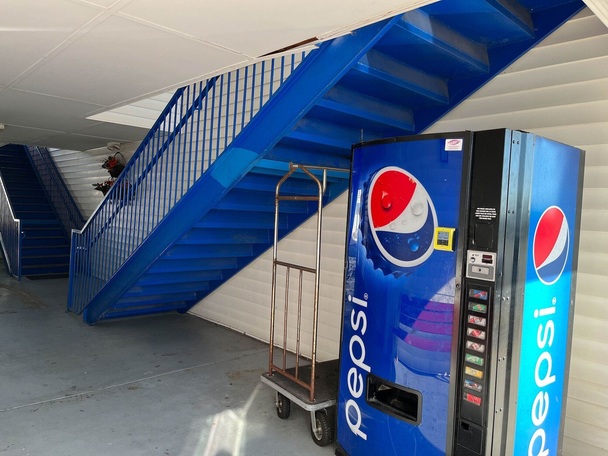 A Pepsi vending machine and a blue staircase in a commercial setting.