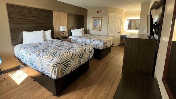 Une chambre d’hôtel avec deux lits, un bureau, un miroir et une petite kitchenette.