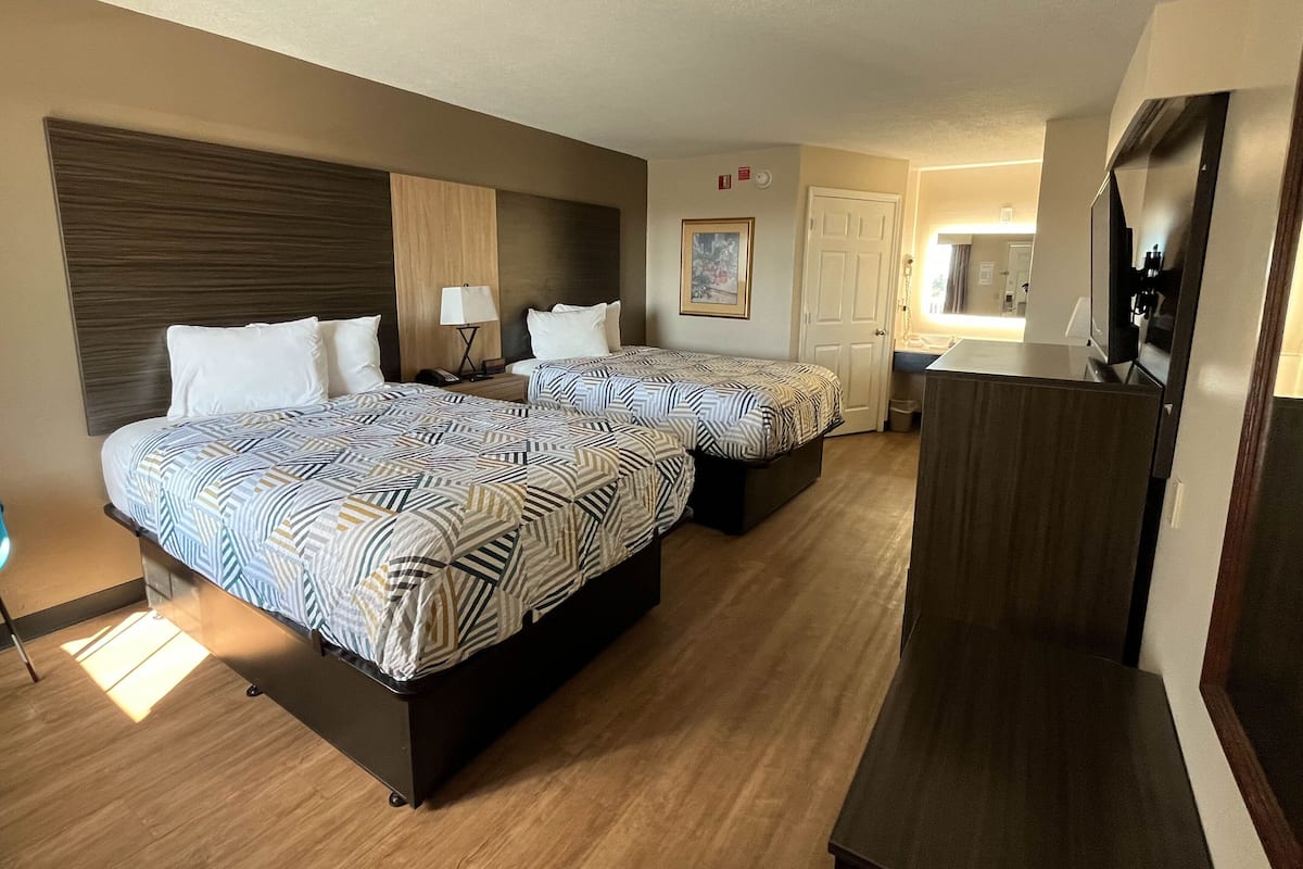 A hotel room with two beds, a desk, a mirror, and a small kitchenette.