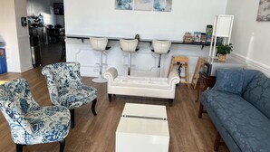 Un salon comprenant un canapé, deux fauteuils à motifs, une table basse blanche et un divan bleu.