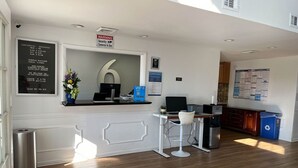 Un espace d’accueil d’hôtel avec un comptoir, un ordinateur et un grand panneau portant le chiffre « 6 ». On y trouve également des panneaux indiquant le petit-déjeuner continental et les frais quotidiens pour les animaux de compagnie.
